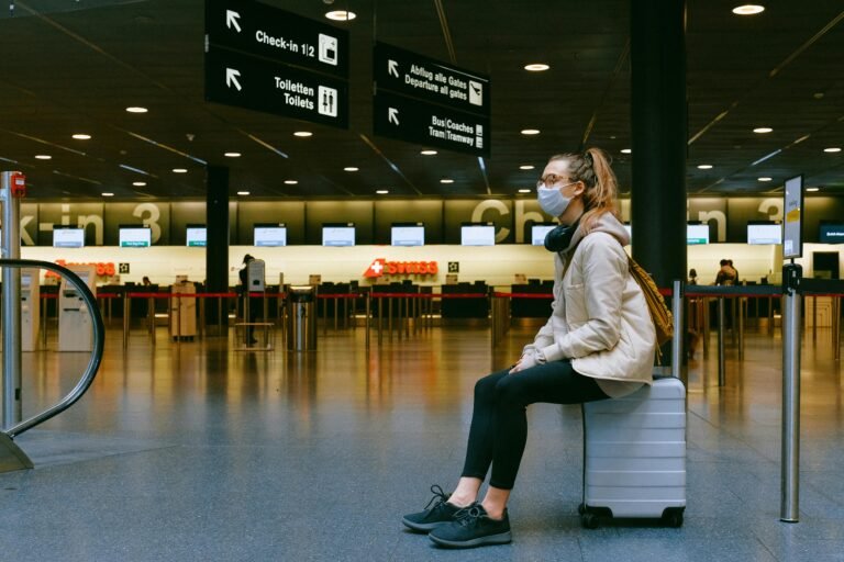 A woman wearing a face mask sits on luggage in an airport terminal amid the pandemic.